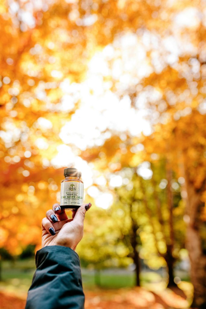 Hand with manicured nails holding CBD oil bottle in fall forest setting.